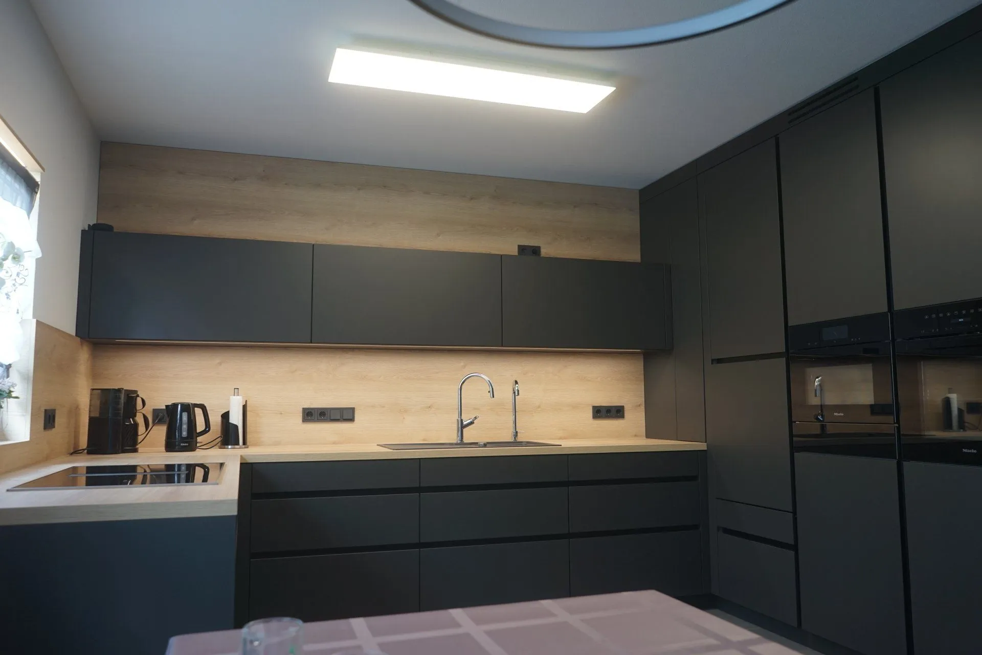 Moderne anthrazitfarbene Einbauküche mit Holzrückwand